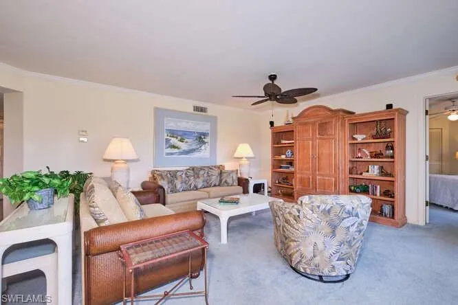 Carpeted living room with ceiling fan, ornamental molding, and visible vents