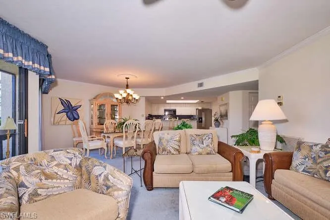 Carpeted living room with an inviting chandelier, visible vents, and crown molding