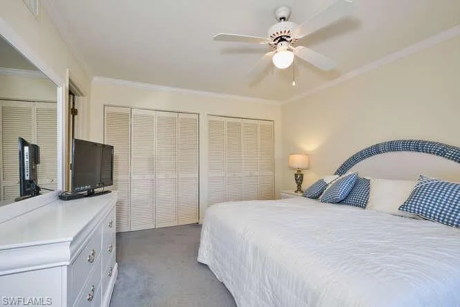 Carpeted bedroom featuring a ceiling fan, crown molding, and two closets