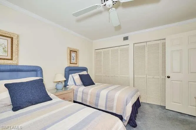 Carpeted bedroom with crown molding, ceiling fan, visible vents, and multiple closets