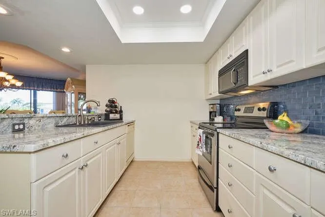 Kitchen with a tray ceiling, electric range, a sink, black microwave, and dishwasher