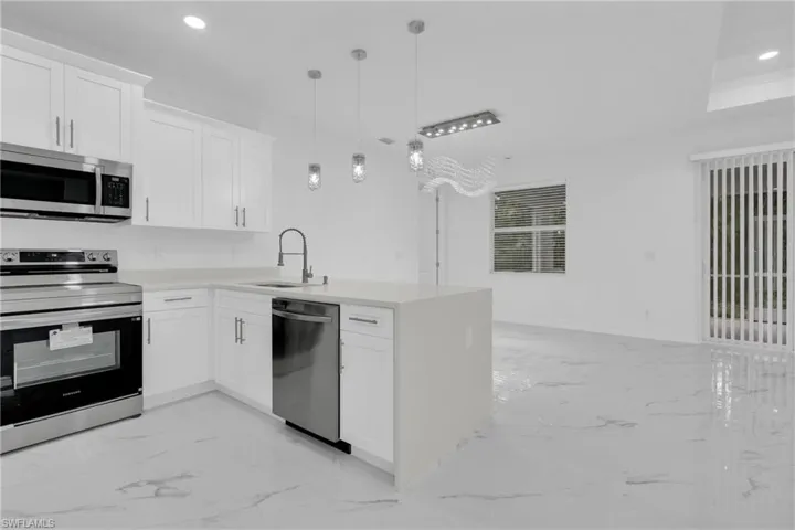 Kitchen featuring appliances with stainless steel finishes, white cabinets, a peninsula, recessed lighting, and light marble finish floors