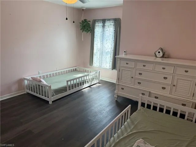 Room featuring dark wood-finish flooring, light-toned walls, and a window with sheer and solid curtains