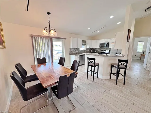 Dining room featuring vaulted ceiling, hanging lights, wood finish floors, and healthy amount of natural light