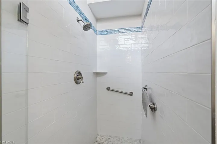 Shower stall with white subway tile walls, a blue mosaic accent band, a built-in shower niche, and brushed nickel fixtures