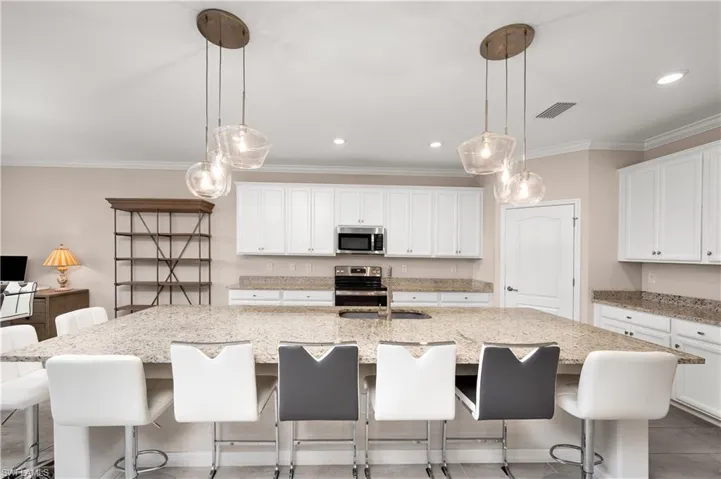 Kitchen featuring hanging light fixtures, appliances with stainless steel finishes, white cabinetry, and a large island
