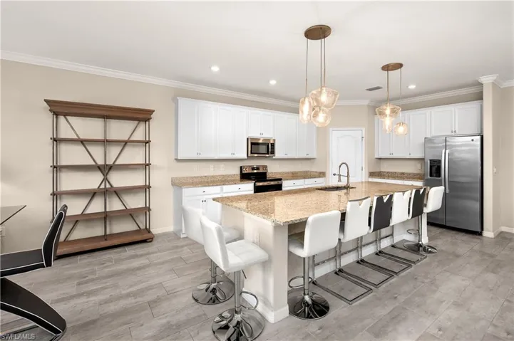 Kitchen featuring white cabinetry, stainless steel appliances, sink, decorative light fixtures, and a center island with sink