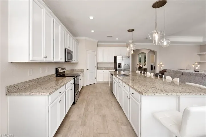 Kitchen featuring a breakfast bar, a large island, stainless steel appliances, decorative light fixtures, and sink
