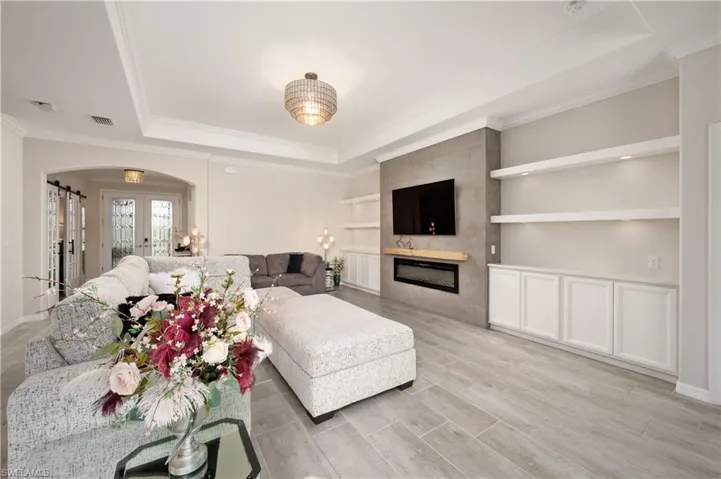Living room featuring a fireplace, french doors, crown molding, built in shelves, and a tray ceiling