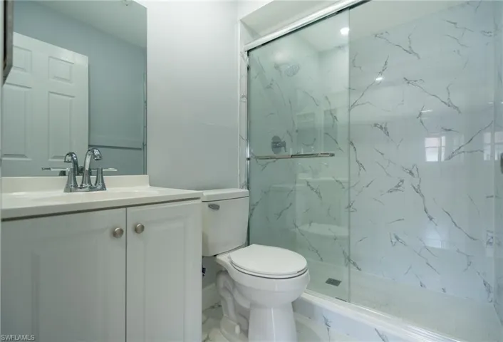 Bathroom featuring a white vanity with integrated sink, chrome faucet, wall-mounted mirror, and a shower with sliding glass doors and white veined wall tile