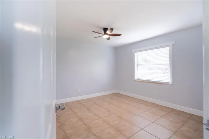 Neutral-toned room featuring ceramic tile flooring, a window with horizontal blinds, and a ceiling fan with integrated lighting