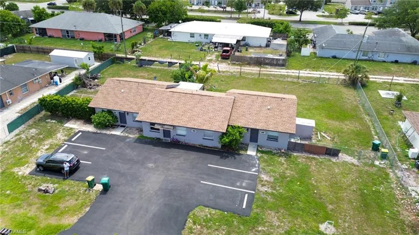 Duplex property featuring a newly paved parking lot with designated spaces, mature landscaping, and light gray exterior siding