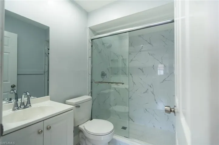 Bathroom with a glass-enclosed shower featuring marble-look wall panels and a sliding door