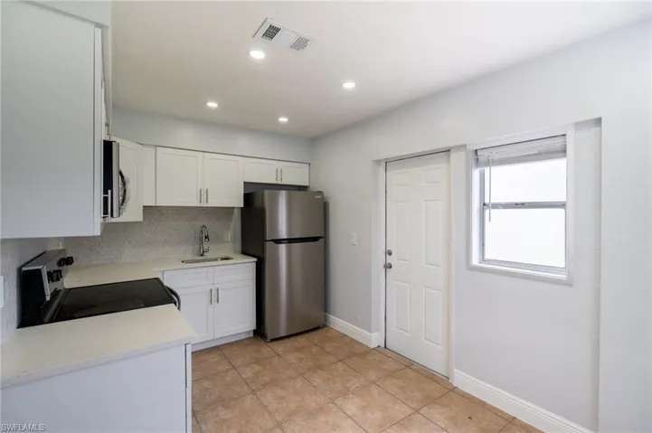 Kitchen featuring white shaker-style cabinetry, stainless steel appliances, light-toned countertops, and a full tile backsplash