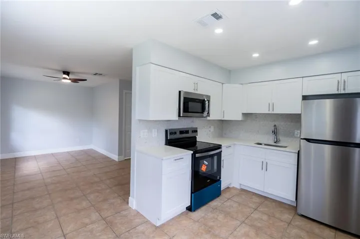Kitchen featuring white shaker cabinetry, stainless steel appliances, light-toned countertops, and a full-height tile backsplash