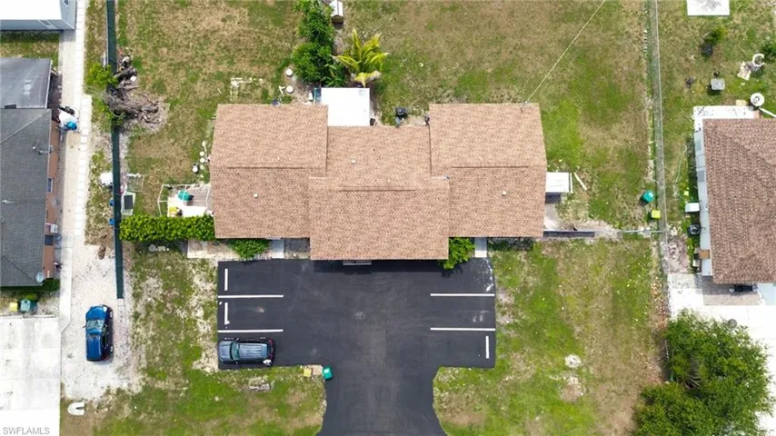 Property featuring a brown shingle roof, paved parking area with marked spaces, and a landscaped hedge