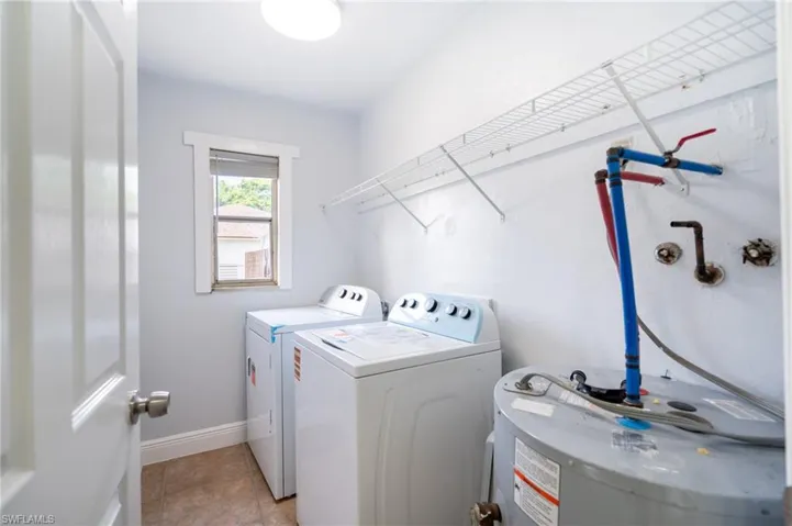 Utility room featuring tile flooring, a window with trim, a water heater, and wall-mounted wire shelving