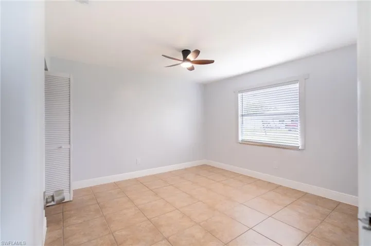 Spacious room featuring tile flooring, a ceiling fan, window with blinds, and louvered closet doors