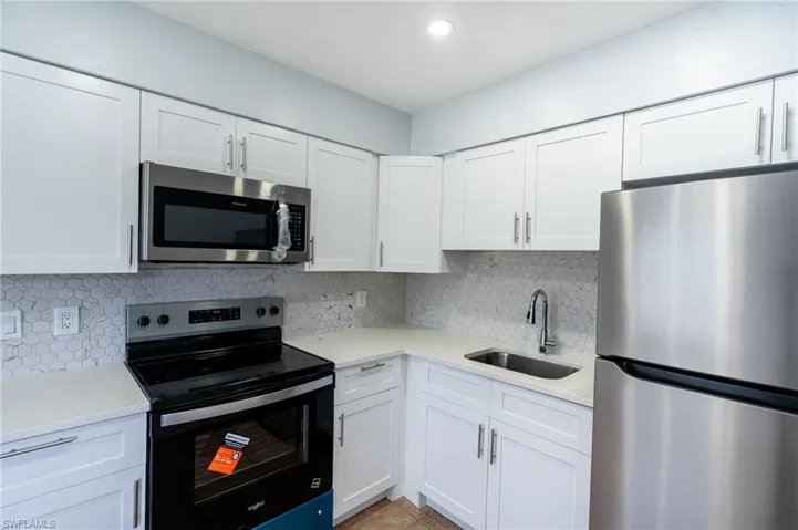 Kitchen featuring white shaker-style cabinetry, light-toned countertops, a geometric tile backsplash, stainless steel appliances, and a stainless steel sink with a gooseneck faucet
