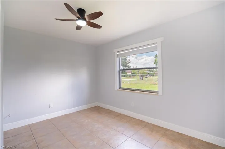 Spacious room featuring neutral tone tile flooring, light-colored walls, a modern ceiling fan with integrated lighting, and a large window with white trim
