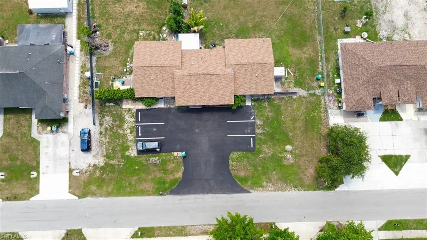 Property featuring a newly paved parking area with marked spaces, a multi-section shingle roof, and surrounding undeveloped green space