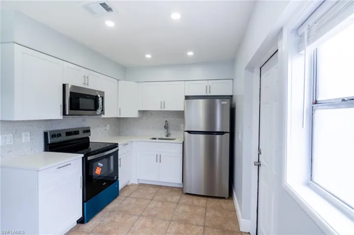 Kitchen featuring white shaker-style cabinetry, stainless steel appliances, light-colored countertops, a mosaic tile backsplash, and tile flooring