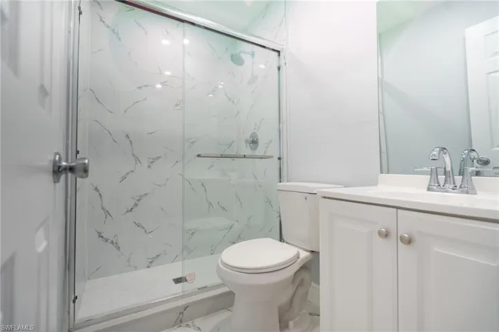 Shower with a sliding glass door, white marble-look wall tiling, and a chrome shower head