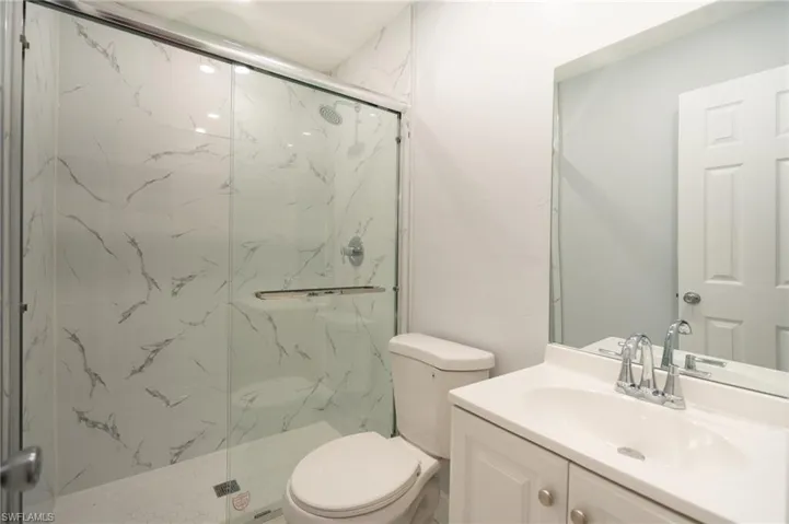 Bathroom featuring a glass-enclosed shower with large format marble-look wall tiling, a white vanity with an integrated sink, a chrome faucet, and a rectangular wall mirror