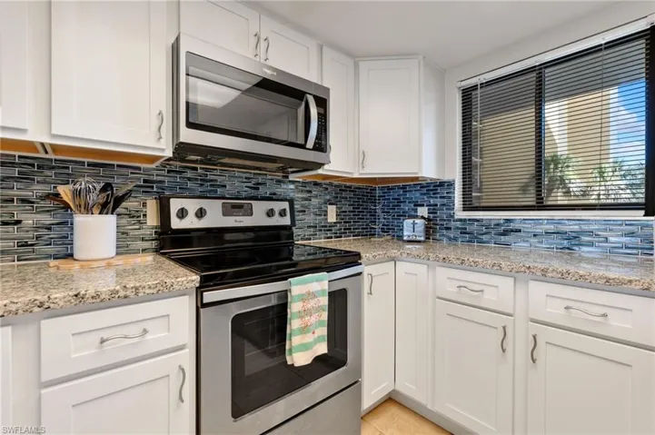 Kitchen featuring appliances with stainless steel finishes, tasteful backsplash, white cabinetry, and light stone countertops