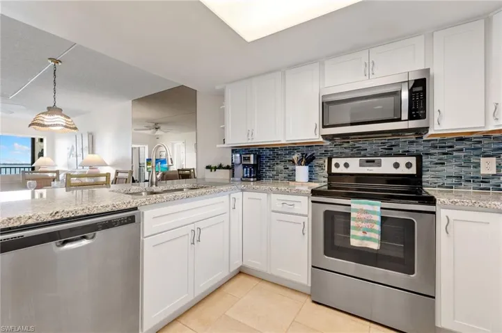 Kitchen featuring appliances with stainless steel finishes, white cabinets, backsplash, light tile patterned floors, and light stone countertops