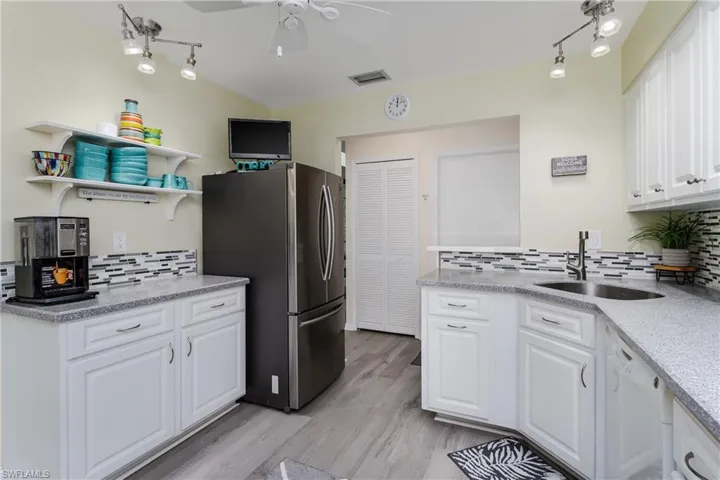 Kitchen featuring white cabinetry, decorative backsplash, light stone countertops, and freestanding refrigerator