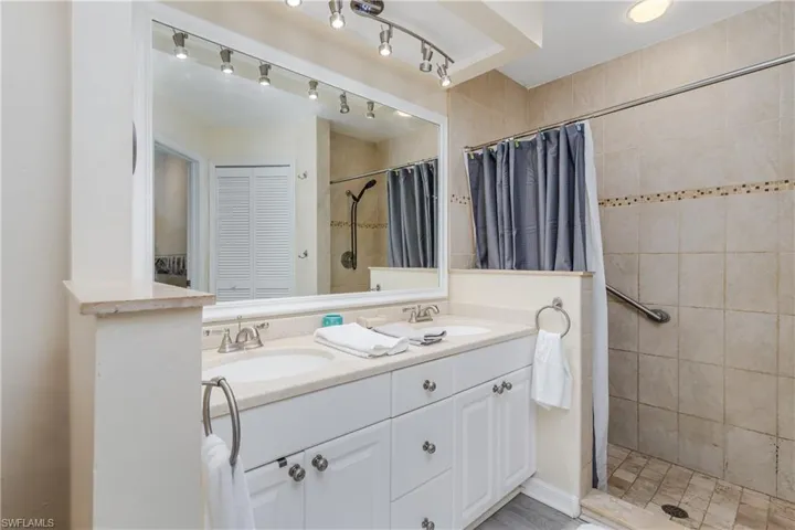 Bathroom with double vanity, a tile shower, and a closet