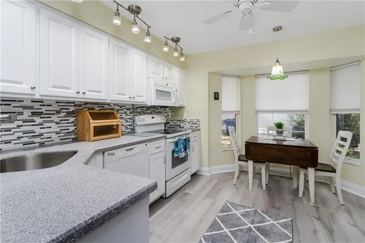 Kitchen with white appliances, white cabinets, light stone counters, tasteful backsplash, and light wood finished floors