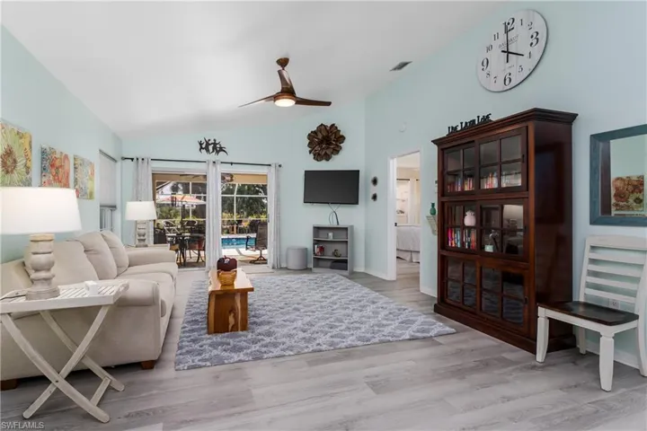 Living room with ceiling fan, light wood-style floors, vaulted ceiling, and a sunroom