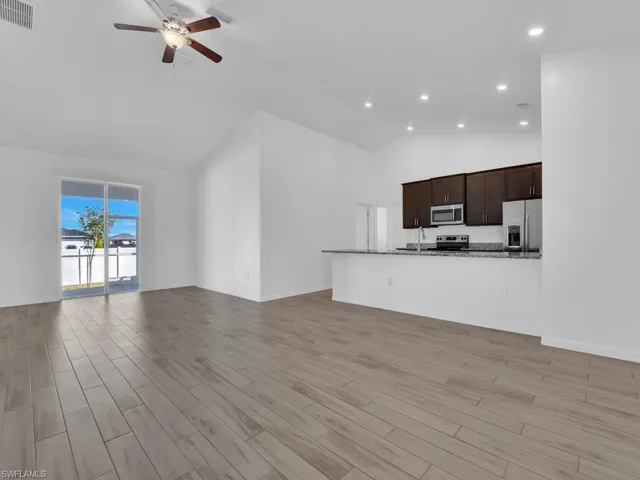 Unfurnished living room with wood tiled floors, vaulted ceiling, a ceiling fan, and recessed lighting