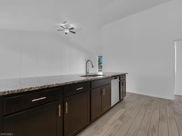Kitchen featuring dark wood finish cabinetry, wood finish floors, a ceiling fan, light stone countertops, and lofted ceiling