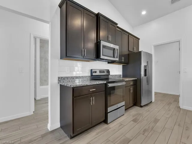 Kitchen featuring stainless steel appliances, dark wood finish cabinets, wood tiled floors, dark stone counters, and vaulted ceiling