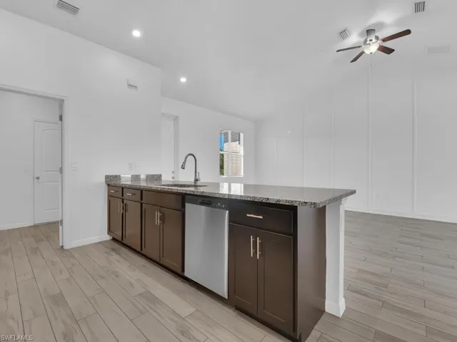 Kitchen featuring dark wood finish cabinets, a peninsula, light wood finished floors, light stone countertops, and lofted ceiling