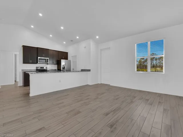 Kitchen featuring open floor plan, dark wood finish cabinets, a peninsula, vaulted ceiling, and stainless steel appliances
