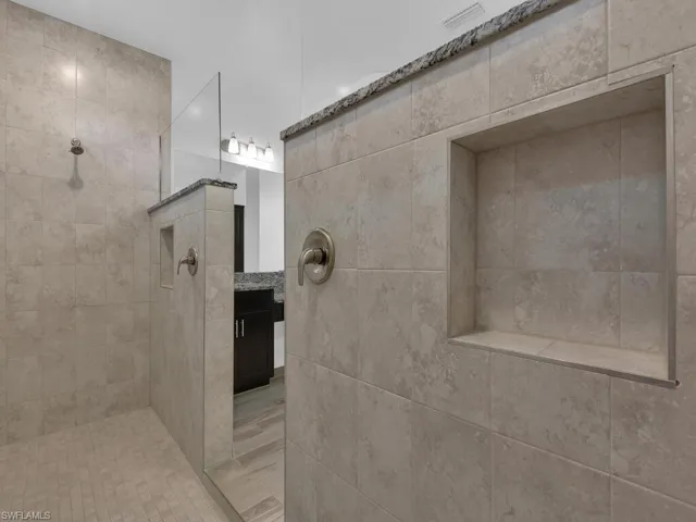 Bathroom featuring a walk in shower, vanity, and tile walls