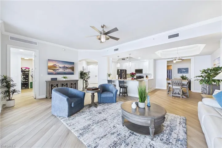 Living area featuring arched walkways, light wood finished floors, ceiling fan, crown molding, and a raised ceiling