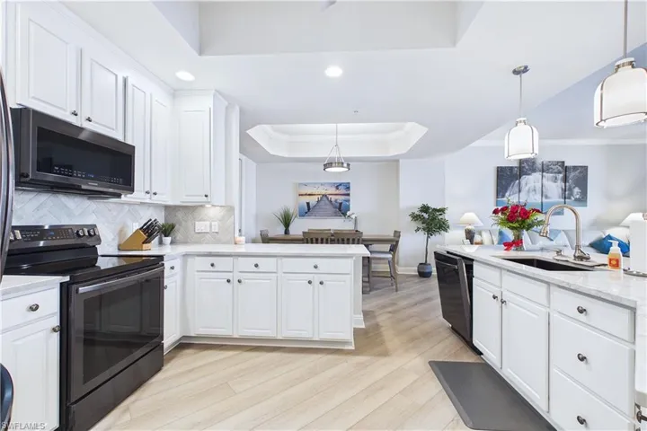 Kitchen with range with electric stovetop, a tray ceiling, white cabinets, light wood-type flooring, and light stone counters