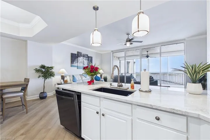 Kitchen featuring crown molding, light stone countertops, light wood-style floors, dishwasher, and white cabinetry
