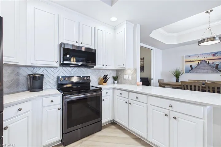 Kitchen with stainless steel appliances, ornamental molding, white cabinetry, light stone countertops, and a raised ceiling