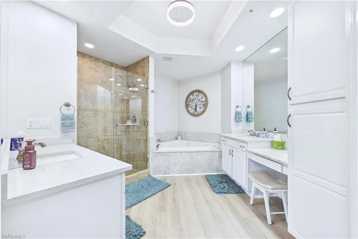 Bathroom with a shower stall, two vanities, light wood-type flooring, a raised ceiling, and recessed lighting