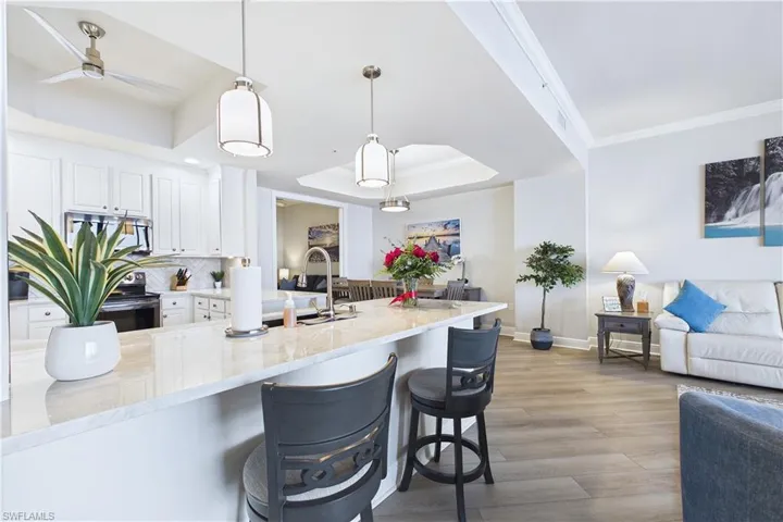 Kitchen with white cabinets, a tray ceiling, hanging light fixtures, light stone countertops, and light wood finished floors