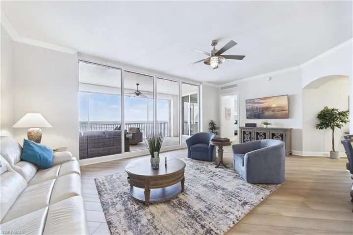 Living area with a ceiling fan, ornamental molding, light wood-style floors, expansive windows, and arched walkways