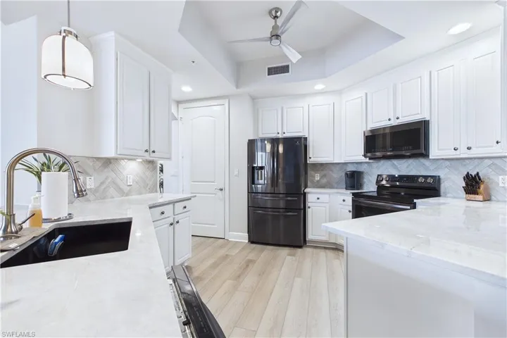 Kitchen with white cabinetry, light stone counters, fridge with ice dispenser, black / electric stove, and light wood-style floors