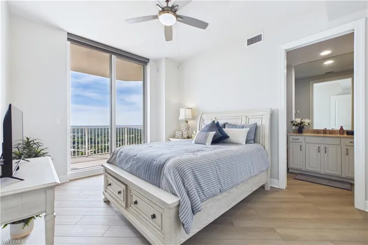 Bedroom with light wood-type flooring, access to outside, connected bathroom, a ceiling fan, and expansive windows