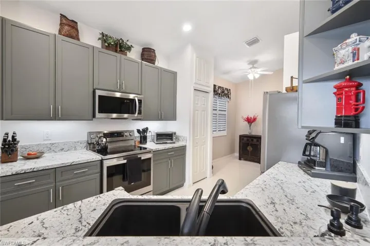 Kitchen with gray cabinetry, light stone countertops, stainless steel appliances, sink, and ceiling fan